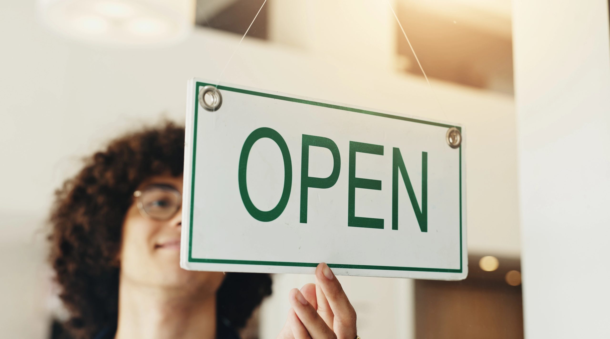 Cafe worker holding an open sign in a small business storefront doorway