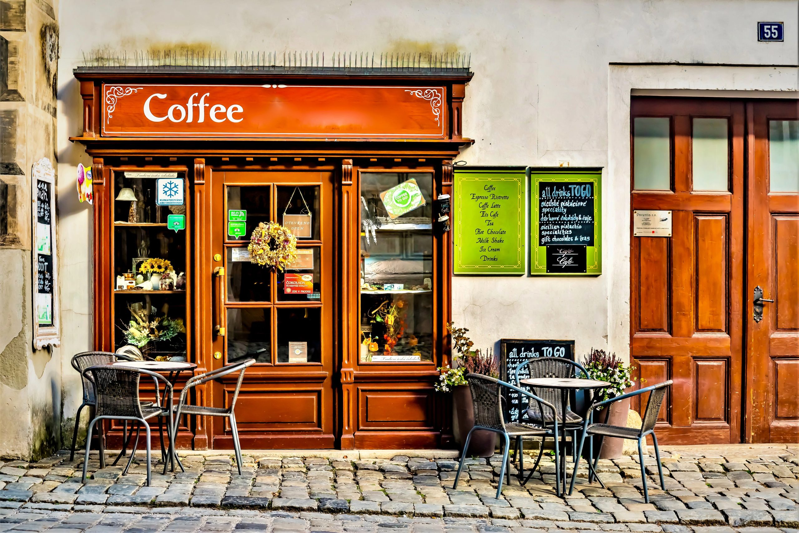 Wooden coffee shop storefront with outdoor tables on a city sidewalk