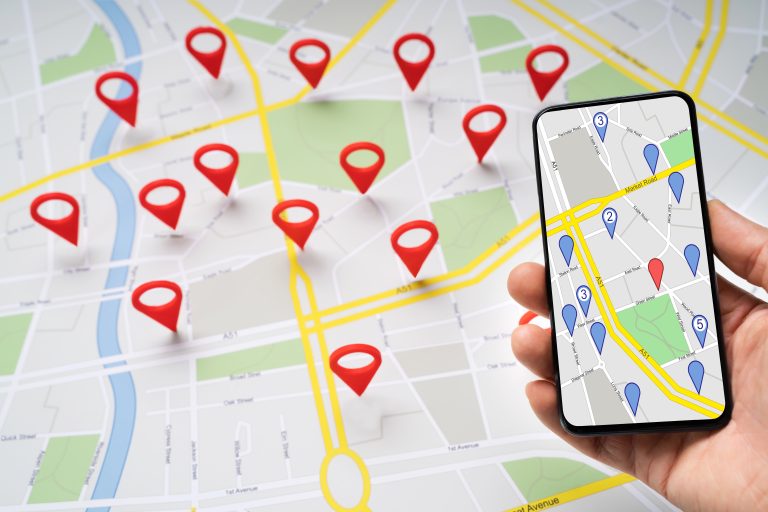 Person holding a smartphone above a road map with red navigation pins