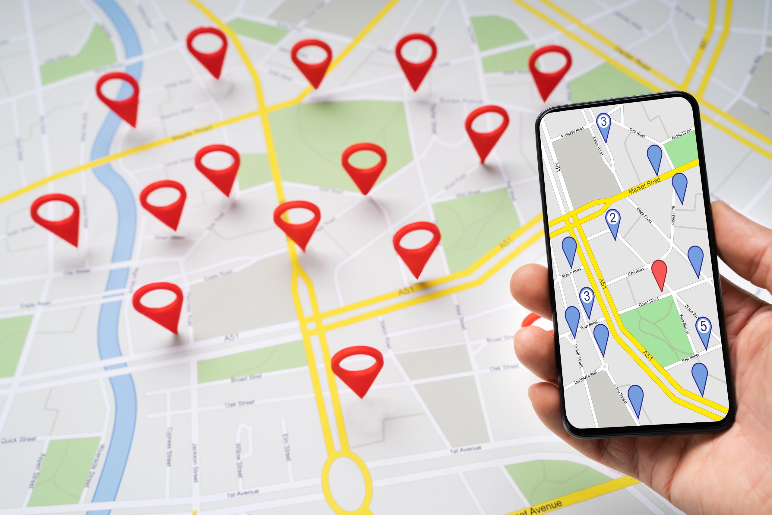 Person holding a smartphone above a road map with red navigation pins